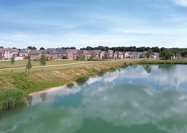 Row of houses near a calm lake with grassy banks and blue sky