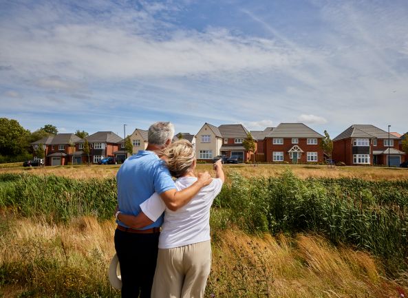Elderly couple looking at houses across a grassy field.